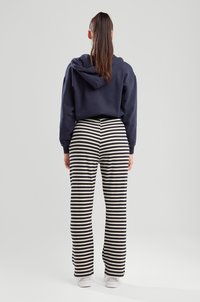 Navy cropped hoodie with a hood, paired with white and navy striped ribbed pants. White sneakers complete the outfit.