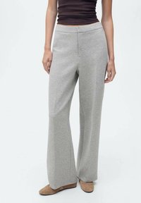 Pantaloni a gamba larga grigi chiari realizzati in tessuto morbido, con vita elasticizzata e dettagli delle cuciture minimi. Abbinati a scarpe color sabbia.
