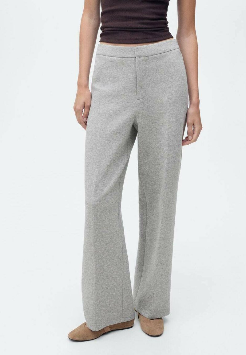 Pantaloni a gamba larga grigi chiari realizzati in tessuto morbido, con vita elasticizzata e dettagli delle cuciture minimi. Abbinati a scarpe color sabbia.