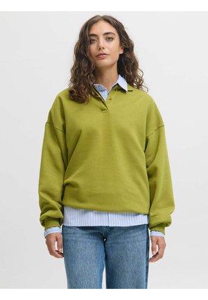 Sweatshirt oversize vert olive avec col, en tissu doux et épaules tombantes, porté par-dessus une chemise à rayures bleues et un jean en denim.