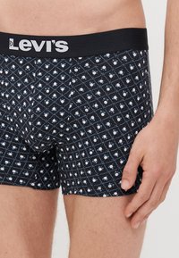 Levi's bokserice v temno modri barvi z belimi in svetlo modrimi vzorci. Imajo črn pas z Levi's logotipom in prilegajočo se zasnovo.