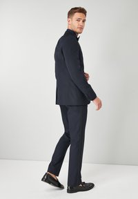 Completo blu con vestibilità su misura, caratterizzato da un giacca a un bottone, pantaloni slim e scarpe nere eleganti per un aspetto formale.