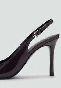 Dámska lodička s vysokým podpätkom a otvorenou pätou v tmavo fialovej lakovej koži, s špicatou špičkou, tenkým podpätkom a nastaviteľným popruhom s prackou. Hladká textúra.