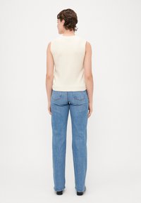 Kremfarget ermeløs strikket topp parret med lyseblå rette jeans. Toppen har rund hals og ribbestrikkede detaljer i kanten.