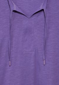 Camicia viola con un tessuto leggero e testurizzato. Presenta una patta frontale e un cappuccio con coulisse con terminazioni abbinate.