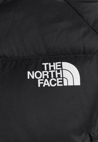 Doudoune noire ornée d'un logo blanc "The North Face". Design matelassé avec une texture lisse et brillante.