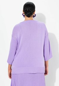 Maglione oversize viola con texture a coste, maniche larghe e cuciture delle spalle scese. Dettaglio notevole: orlo a strati.