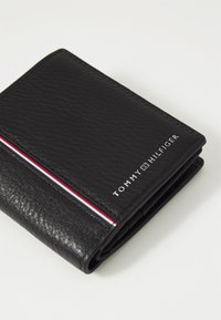 Must musträkiga rahakott mustast nahast. Omab punase ja valge triibulist detaili ning hõbedaselt reljeefset "TOMMY HILFIGER" logo.