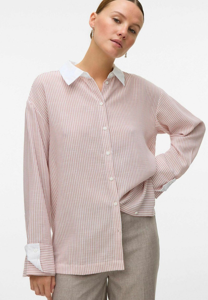 Button-up skjorta med vertikala röda och vita ränder, långa ärmar, vit krage och uppvikta manschetter. Tillverkad av lättviktsmaterial.
