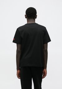 Mustast puuvillast valmistatud lühikeste varrukatega t-särk. Omadusteks on ümar kaelus, lõdvalt istuv lõige ja vasakul varrukal väike punane logo detail.