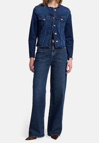 Tummansininen farkkutakki, jossa on tiukka malli, etutaskut ja napitus. Yhdistetty leveälahkeisiin tummansinisiin farkkuihin.