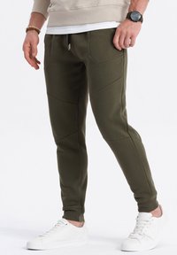 Olijfgroene jogpants in een aansluitend ontwerp met textuurpanelen, elastische boorden en trekkoordsluiting. Gepaard met witte sneakers.