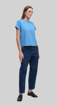 Niebieska bawełniana koszulka z krótkim rękawem, zestawiona z jeansami o wysokim stanem w ciemnym odcieniu i czarnymi mokasynami; prosta, casualowa stylizacja.