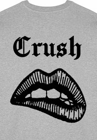 Pelēks auduma T-krekls ar lielu melnu grafiku, kurā attēlotas lūpas ar atvērtu muti, virs kurām ir vārds "Crush" blīvā, gotiskā fontā.