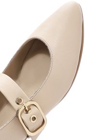 Zapato Mary Jane de cuero beige con punta redonda, una correa ajustable con un hebilla dorada y textura suave.