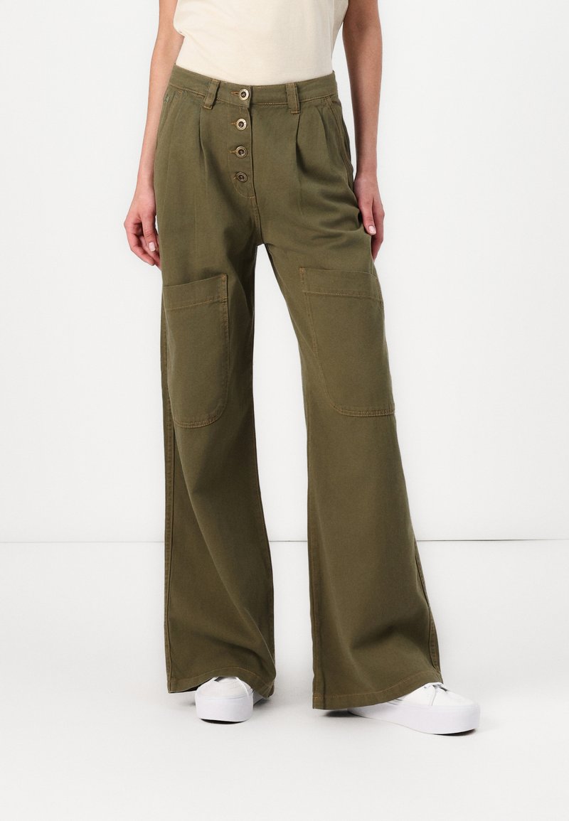 Ces pantalons large olive ont un devant à boutons avec quatre grands boutons. Ils possèdent deux poches latérales substantielles et un tissu texturé.
