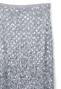 Tissu en sequins argentés avec une doublure en maille, présentant une surface texturée et des accents brillants. Le motif a une trame lâche.