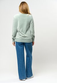 Gr ön, mjuk sweatshirt med ribbade manschetter, i kombination med vida blå denimjeans. Enkel, avslappnad design utan synlig märkning.