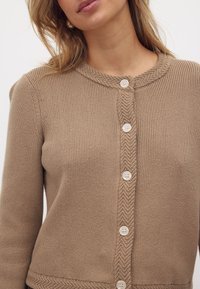 Beige gebreide cardigan met een ronde hals, een textuurpatroon en vijf knoopsluitingen aan de voorkant.