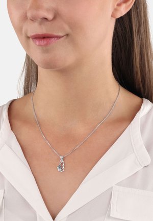 Donna che indossa una collana di metallo argento con un pendente a forma di farfalla, vestita con una camicetta bianca a colletto a V.