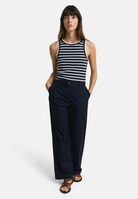 Marineblå vide benbukser parret med en marineblå og hvid stribet ærmeløs top. Outfitet har en knapdetalje og en afslappet pasform.