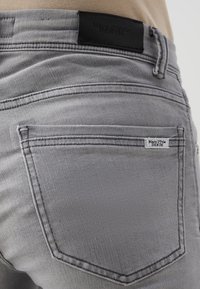 Jeans de mezclilla gris con una etiqueta de cuero en la parte trasera de la cintura, costuras mínimas y una pequeña etiqueta de la marca cerca del bolsillo trasero.