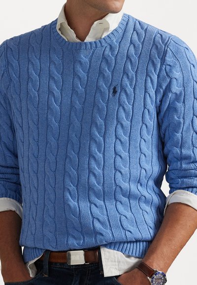 Pull en tricot bleu clair avec un motif en côtes, doté de poignets et d'un ourlet côtelés, avec un petit logo sur la poitrine et superposé sur une chemise blanche à col.
