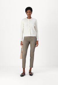 Vit texturerad kofta med rund hals, knappfront, parat med beige smal passform på anklarna och svarta platta skor. Handväska i beige som accent.