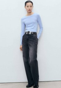 Ljusblå långärmad topp kombinerad med mörkgrå high-waisted jeans. Har ett silverbälte med rektangulär spänne och stiliga svarta skor.