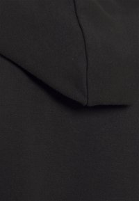 Tessuto di felpa nera in cotone che mostra un primo piano della superficie testurizzata, con un dettaglio del colletto piegato sul bordo superiore.