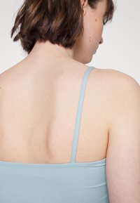 Camisola azul claro com alças finas, apresentando uma textura suave e um design ajustado, vista pela parte de trás.
