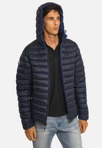 Veste matelassée bleu marine avec capuche, design matelassé, fermeture éclair à l'avant et poches latérales. Le matériau semble brillant et isolant.