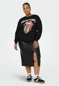 Melna sporta krekla ar Rolling Stones grafiku, melna mākslīgā āda svārki ar šķirbu, un brūni sporta apavi ar baltajiem akcentiem.