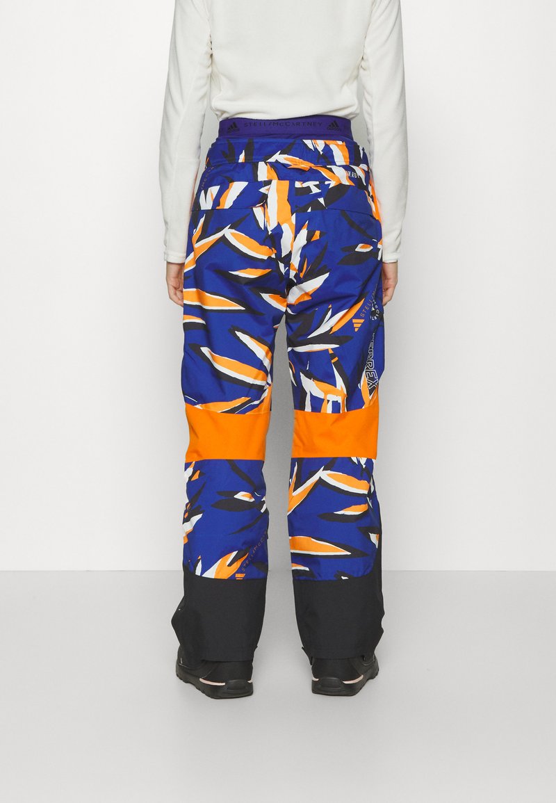 Pantaloni da neve multicolore con un design blu e arancione e motivi audaci. I pantaloni hanno una cintura elastica e polsini neri alle caviglie.