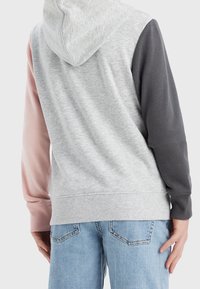 Felpa con cappuccio di colore grigio chiaro, manica sinistra rosa e manica destra grigio scuro. Texture liscia con polsini e orlo a coste.