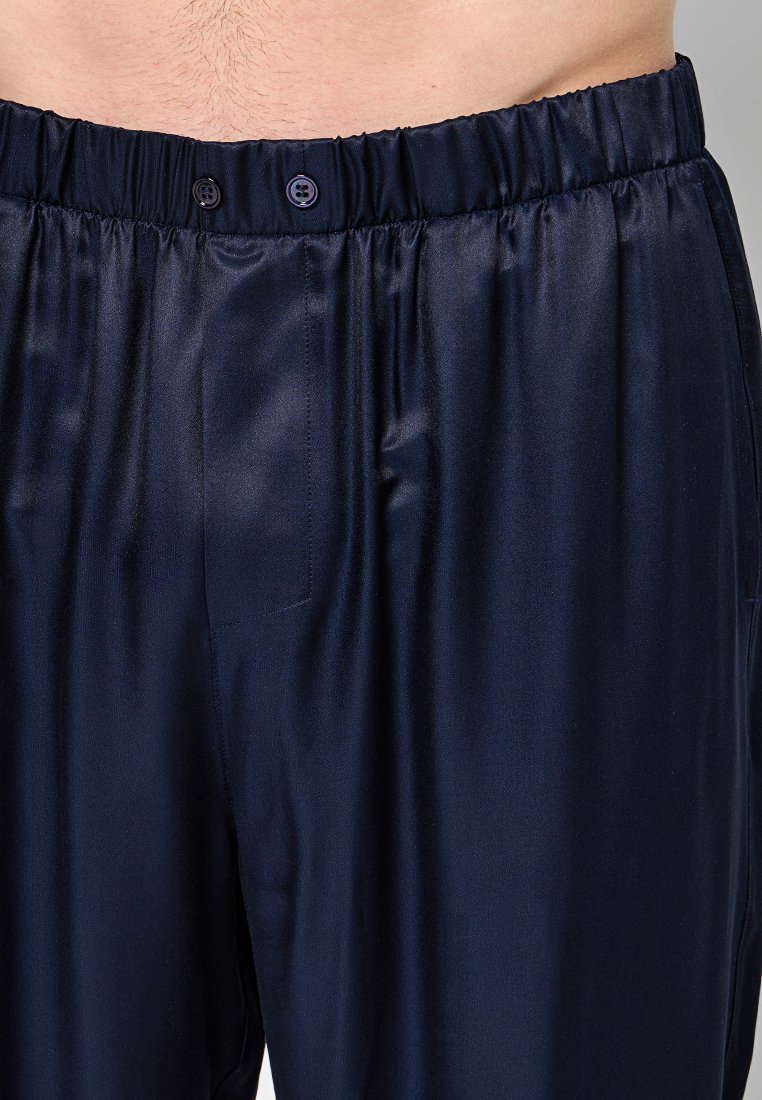 Shorts de nuit en satin bleu marine avec taille élastique, dotés d'une fermeture à bouton et d'une texture lisse. Poche latérale visible sur la gauche.