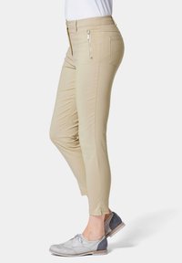 Beige slim-fit broek met een gladde textuur, zijrits zakken en een taps toelopend ontwerp, gecombineerd met grijs en blauwe veterschoenen.