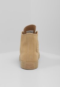 Béžové semišové vysoké tenisky s kulatou nášivkou, texturovaným povrchem a gumovou podrážkou. Na patě se nachází značení "CONVERSE ALL★STAR".