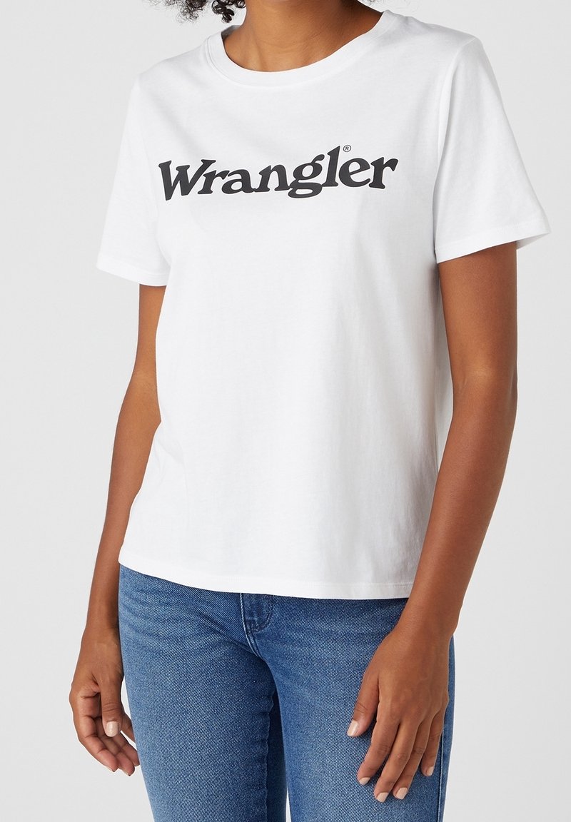 Bílý bavlněný tričko s krátkým rukávem, kulatým výstřihem a velkým černým logem "Wrangler" přes hrudník. Měkká textura, volný střih.