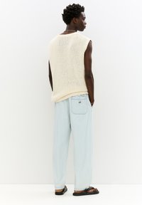 Ljus beige stickad ärmlös topp med löst sittande passform, kombinerad med blekblå baggy jeans med bakficka och logotagg. Sandaler fulländar looken.
