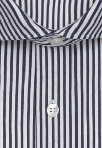 Chemise blanche à rayures verticales bleu marine, avec col boutonné et bouton blanc visible sur la patte de boutonnage avant.