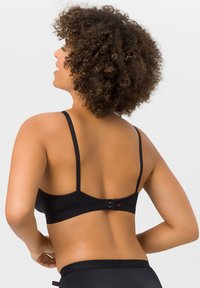 Black bra featuring thin adjustable straps, a smooth texture, a hook-and-eye closure at the back, and a small pink logo detail.