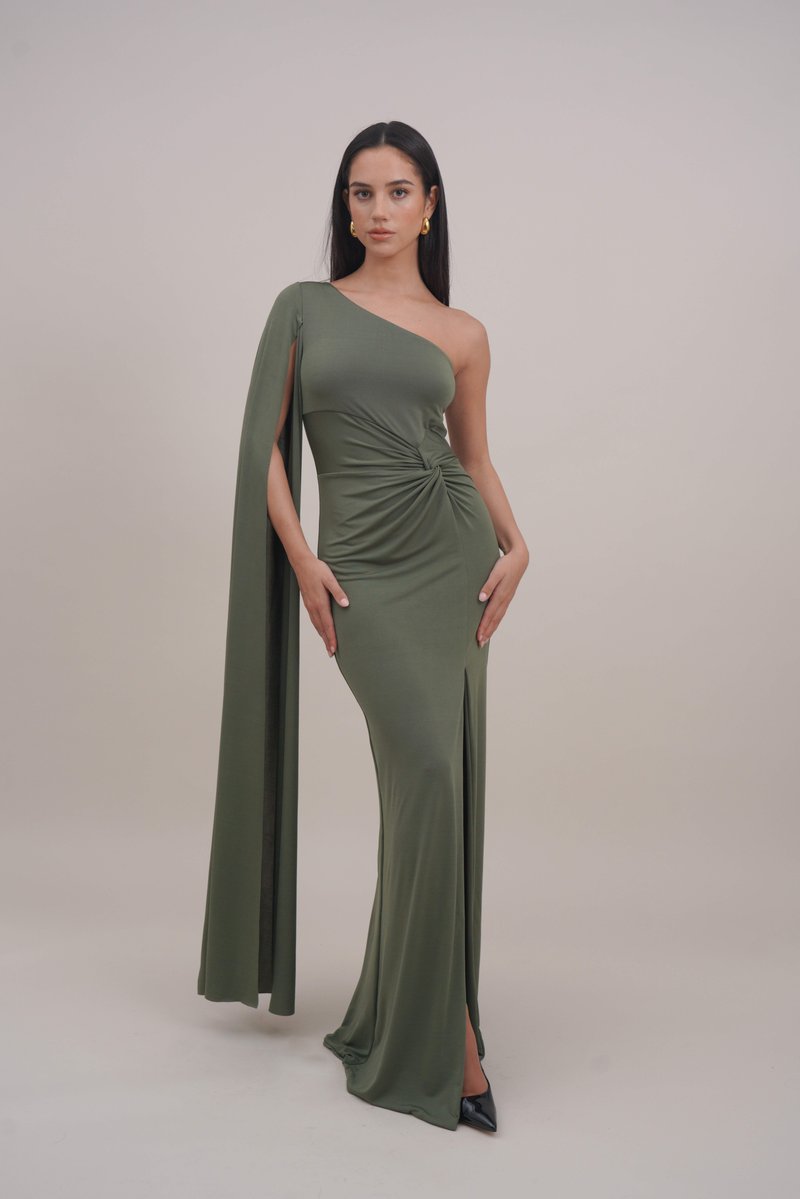 One-shoulder olive green gown with a fitted silhouette, draped cape sleeve, and side slit. Smooth fabric with gathered detail at the waist.