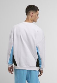 Felpa bianca con pannelli laterali blu e neri, design oversize, tessuto texturizzato, collo a giro e maniche scese.