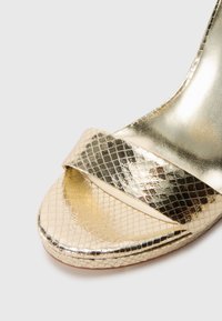 Goldener High-Heel-Sandale mit einem strukturierten Schlangenledermuster im Obermaterial. Verfügt über einen breiten Riemen und eine glatte, geschwungene Sohle.
