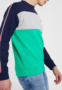 Vihreä, laivastonsininen ja harmaa väriblokkipusakka, jossa on ribbireunat, py�öreä kaula-aukko ja raidalliset yksityiskohdat hihoissa. Valmistettu pehmeästä puuvillasekoitteesta.