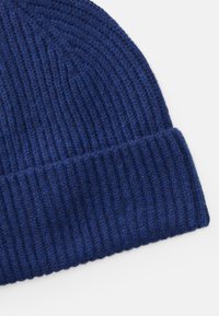 Knit blue wool beanie with a ribbed texture, featuring a folded brim and a slightly dome-shaped top. Soft and warm material.