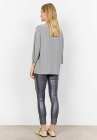 Top gri tricotat cu mâneci trei sferturi, purtat cu colanți gri lucioși și pantofi joși de culoare deschisă. Fundal simplu, design minimalist.