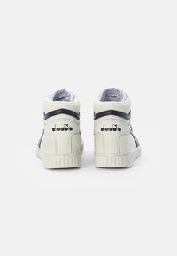 Baskets montantes avec un extérieur en cuir blanc, des accents bleu marine, une semelle en caoutchouc texturée et un logo de marque à l'arrière.