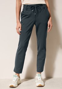Pantalones de chándal gris oscuro con cintura elástica y cordón, con bolsillos laterales y piernas ajustadas, combinados con zapatillas de color claro.